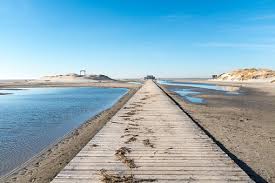 Boardwalk yang panjang mengarah ke pantai berpasir.